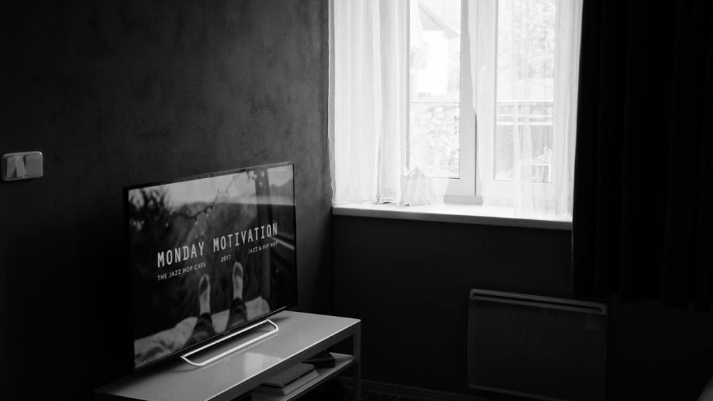 Black and white photo of a modern interior featuring a TV and window with sheer curtains.